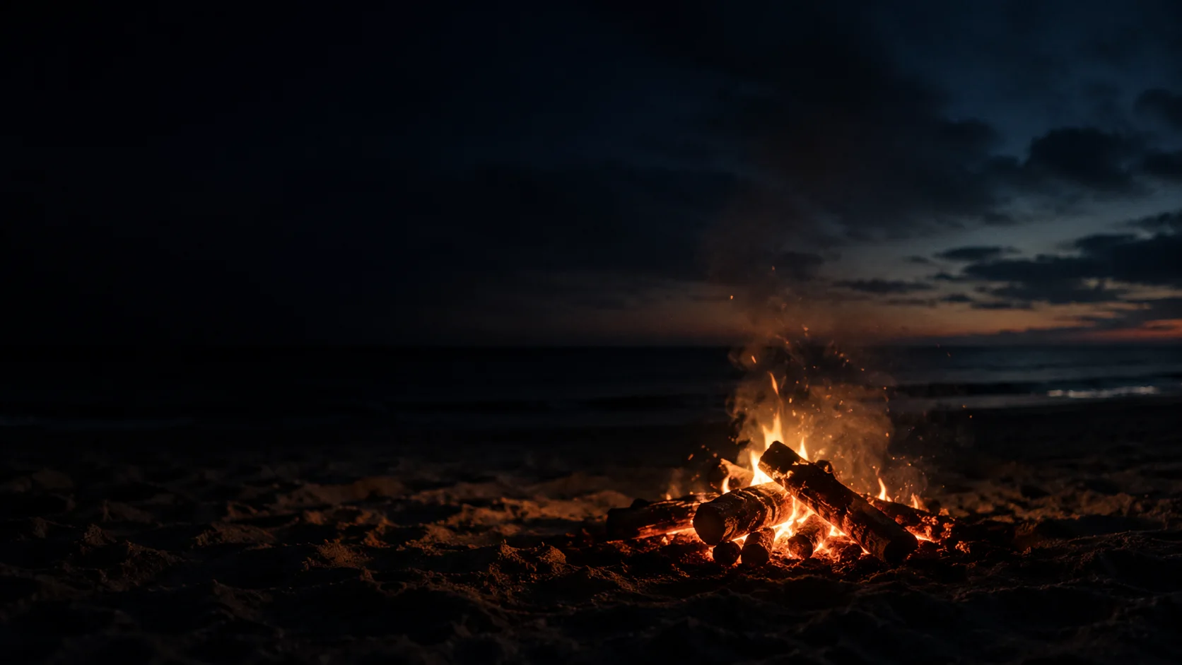 Spiaggia deserta di notte, un falò di braci in lontananza